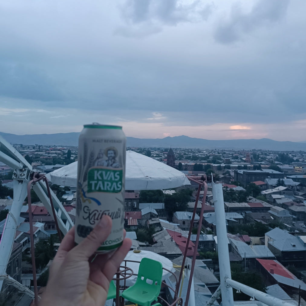 Hand holding a can of Kvas Taras against a cityscape with mountains in the background